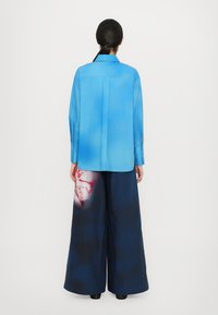 Blue shirt with a fading gradient, long sleeves, and a pointed collar paired with wide-leg navy trousers featuring a floral print.