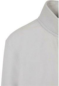 Pehmeä harmaa fleece-mock-neck-paita. Pehmeä rakenne, jossa on hienoinen kiilto, ja joka sisältää muotoillun kauluksen sekä brodeeratut yksityiskohdat reunoilla.