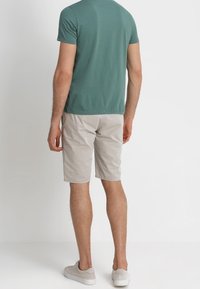 Vihreä lyhytningallinen paita yhdistettynä vaaleisiin shortseihin, jotka näyttävät normaali istuvuudelta ja sileältä kankaalta. Kenkien väri on vaaleanharmaa ja niissä on yksinkertainen muotoilu.