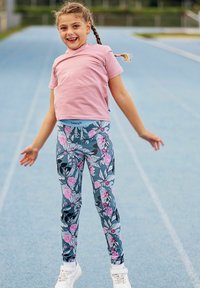 Jasnoróżowa koszula z krótkim rękawem w połączeniu z legginsami w szarym i różowym kwiatowym wzorze. Białe sneakersy dopełniają sportowy strój.