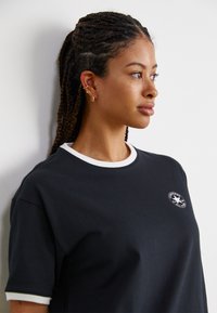 Μαύρη μπλούζα με λευκό γιακά και μανίκια, με κυκλικό λογότυπο Converse στο στήθος. Μαλακό ύφασμα με χαλαρή εφαρμογή.