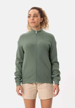 Groene zip-up jas met een textuurpatroon, hoge kraag en ribgebreide manchetten, gecombineerd met beige shorts.