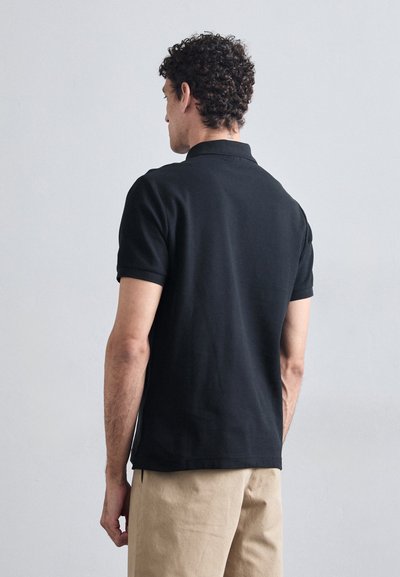 Camisa polo negra con cuello clásico y mangas cortas, hecha de tela suave. Presenta un dobladillo recto y detalles de costura sutiles.