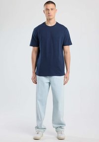 Tummansininen puuvillapaita, jossa on pyöreä kaula-aukko, yhdistettynä vaaleansinihin väljiin farkkuihin ja valkoisiin lenkkareihin. Yksinkertainen muotoilu, ei näkyviä kuvioita.