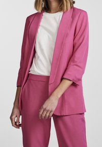 Veste rose à coupe décontractée et ouverture devant, avec manches trois-quarts et poches latérales, associée à un pantalon assorti et ajusté.