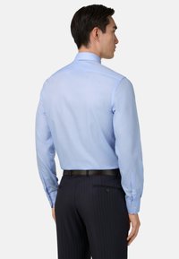 Svetlo modra, s dolgimi rokavi, srajca z gladko teksturo, z gumbi na manšetah in slim fit krojem, v kombinaciji s temnimi hlačami z drobnim prugastim vzorcem.