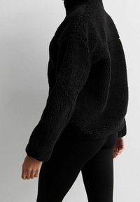 Czarny polarowy półgolf o wysokim kołnierzu, fakturowanej powierzchni i opuszczonych ramionach. W zestawie z czarnymi legginsami. Miękki i przytulny design.