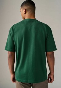 Camiseta verde de manga corta con un corte holgado, hecha de algodón. Sin patrones visibles. Color sólido con cuello redondo y dobladillo recto.