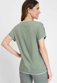 Light green short-sleeve shirt with a relaxed fit, round neckline, and contrasting teal trim along sleeves and hem. Smooth texture and minimal design.