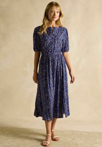 Modrá kvetinová maxi šaty s krátkymi puff rukávmi, so zberaným pásom a gombíkovým zapínaním vpredu. Tkanina obsahuje podrobný vzor v kontrastných farbách.