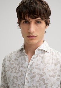 Kurzärmeliges, weißes Hemd mit leicht beigem Blumenmuster, mit Kragen und durchgehendem Knopfverschluss. Hergestellt aus einem leichten, strukturierten Stoff.