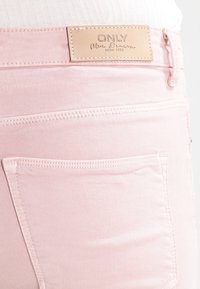 Lichtroze denim jeans met een leren label met de tekst "ONLY Blue Denim" en zichtbare stiksels, inclusief een achterzak.