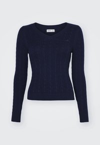 Marinblå kabelstickad tröja med V-ringning och långa ärmar, figursydd silhuett, med en subtil broderad logotyp på bröstet.