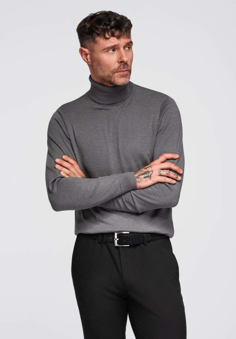 Maglione grigio a collo alto con maniche lunghe, realizzato in tessuto morbido, abbinato a pantaloni neri e una cintura nera con fibbia argentata.