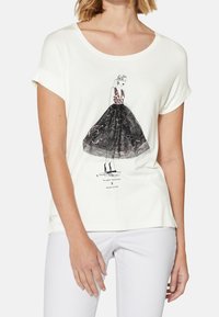 Camiseta blanca de manga corta con un gráfico de una mujer en un vestido negro de encaje con un estampado texturizado, cuello redondo y mangas enrolladas.