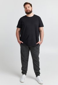 Fekete rövid ujjú póló sötétszürke jogger nadrággal párosítva. A nadrág oldalán zsebek találhatók és gumírozott szegélyek, fehér tornacipővel kiegészítve.