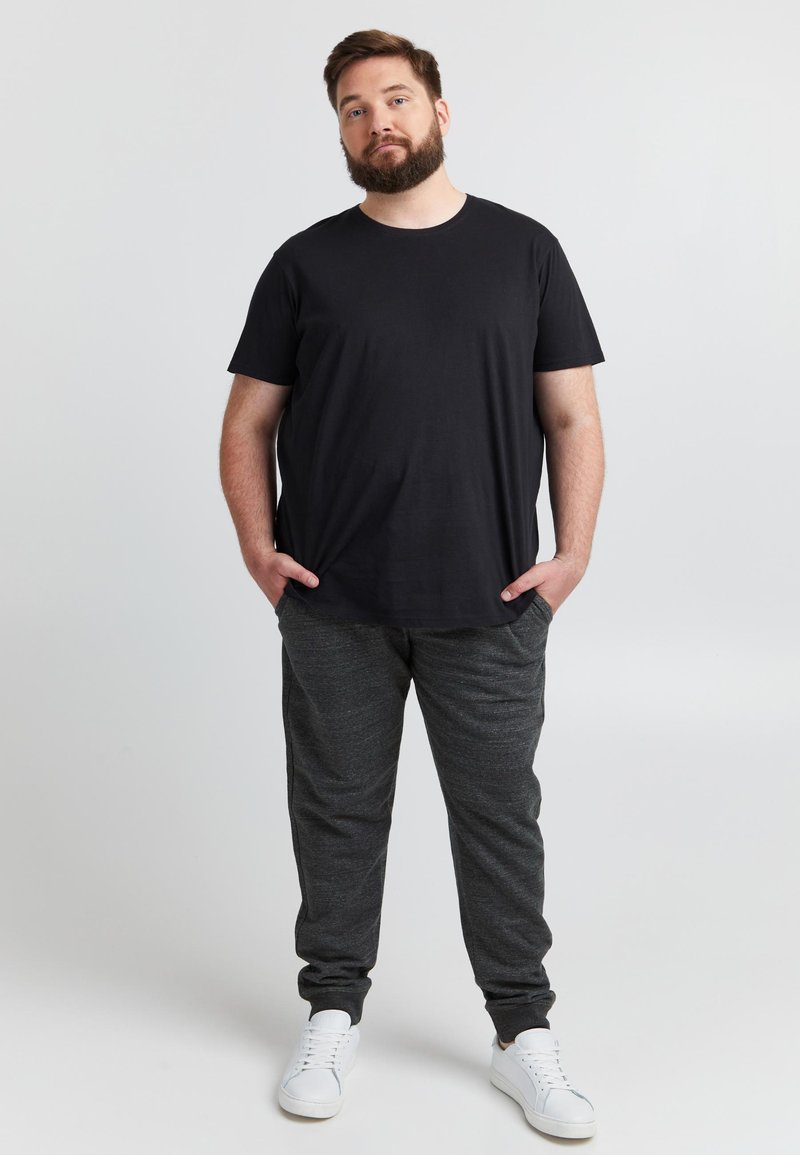 Fekete rövid ujjú póló sötétszürke jogger nadrággal párosítva. A nadrág oldalán zsebek találhatók és gumírozott szegélyek, fehér tornacipővel kiegészítve.