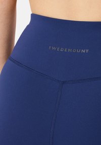 Marinblå högmidjade leggings i elastisk tyg, med en elegant design med matt yta och SWEDEMOUNT-logotyp nära midjan.