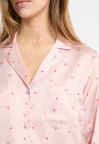 Parte superior de pijama rosa claro con rayas sutiles, con un patrón de copas de cóctel y cerezas. Incluye un bolsillo en el pecho y cuello clásico.