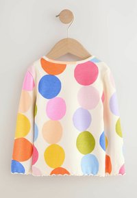 Haut à manches longues avec une texture côtelée, orné de pois colorés (rose, bleu, orange, vert) sur un fond crème, et doté d'un ourlet festonné.