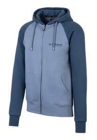 Felpa con zip, corpo azzurro chiaro e maniche raglan blu scuro. Presenta due tasche frontali e cordini. Il materiale è morbido e con texture.