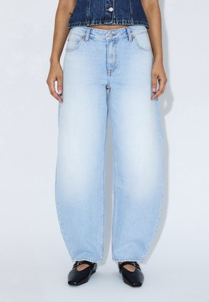 Jeans bleu clair à jambes larges avec une finition délavée, conception classique à cinq poches, coutures surpiquées, et taille haute. Portés avec des ballerines noires.