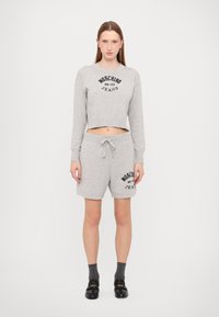 Sweatshirt cinzento cropped com impressão de logótipo preto, combinado com calções cinzentos correspondentes com uma cintura elástica e detalhe do logótipo. Calçado preto.