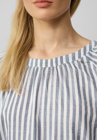 Blusa a righe blu e bianche con scollatura rotonda e dettagli arricciati sulle spalle, realizzata in un tessuto leggero e strutturato.
