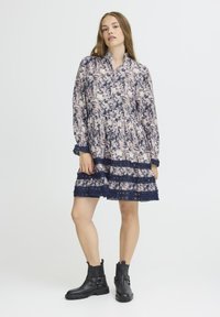 Zilā un krēmkrāsas garām piedurknēm ziedu kleita ar mežģīņu akcents un pakāpenisku dizainu. Valkāta ar masīvām melnām potīšu zābakiem.