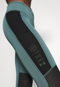 Tummansininen ja mustat leggingit, joissa on korkea vyötärö, verkkopaneelit, kontrastiväriset ompeleet ja logo yksityiskohtina sivuilla.