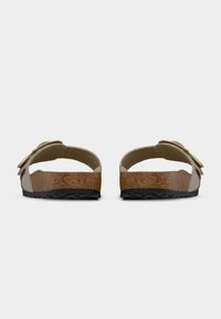 Μπεζ σουέντ σανδάλια τύπου slip-on με πάτο από φελλό, μαύρη υφασμένη σόλα και χρυσή αγκράφα σε ρυθμιζόμενο λουράκι, εμφανιζόμενα από πίσω όψη.