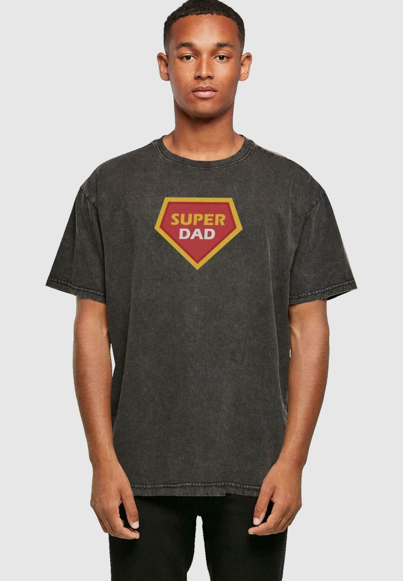 Zwarte vervaagde katoenen t-shirt met een grote rode en gele "SUPER DAD" graphic in de vorm van een schild aan de voorkant, met een relaxte pasvorm.