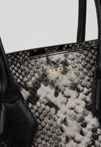 Svart och grå tote-väska i konstläder med orm-utseende, som har texturerade detaljer, släta kanter och guld "ALDO" branding på sidan.