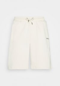 Shorts de sport couleur crème en tissu doux. Ils comportent une taille élastique avec cordon de serrage et un logo discret sur la cuisse gauche.