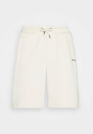 Cream-colored athletic shorts in soft fabric. Features an elastic waistband with drawstring and a subtle logo on the left thigh.