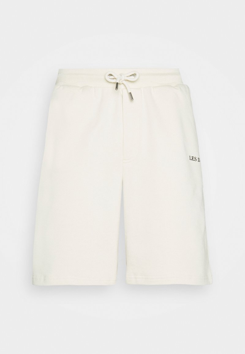 Shorts de sport couleur crème en tissu doux. Ils comportent une taille élastique avec cordon de serrage et un logo discret sur la cuisse gauche.