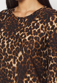 Abito a stampa leopardata con texture plissettata, scollatura rotonda e una palette di colori che include nero, marrone e crema. Tessuto morbido con una leggera lucentezza.