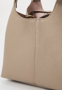 Beige leather handbag with a textured surface, curved shape, and visible stitching. Features a gold hardware accent near the top.