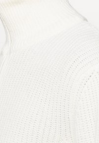 Pull col roulé en maille blanche avec un motif côtelé texturé, doté d'un col haut et d'un tissu doux et léger.