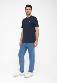 Dunkelblaues Baumwoll-T-Shirt mit Rundhalsausschnitt und kurzen Ärmeln, kombiniert mit hellblauen Jeans und weißen Sneakers mit einem grauen Logo.