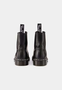 Paire de bottines en cuir noir avec semelles épaisses en caoutchouc et languettes portant l'inscription « WITH BOUNCING SOLES », vues de dos sur fond blanc.