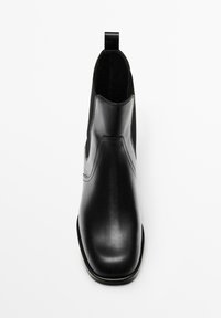 Bottine en cuir noir avec bout pointu, panneaux latéraux élastiques et languette à l'arrière. Texture lisse et design élégant.