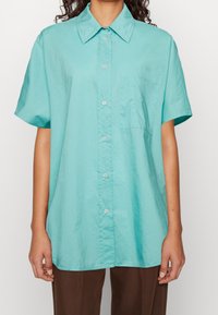 Camicia a maniche corte color turchese chiaro con collo a punta, taschino sul petto e tessuto di cotone liscio.