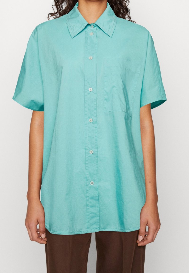 Camicia a maniche corte color turchese chiaro con collo a punta, taschino sul petto e tessuto di cotone liscio.
