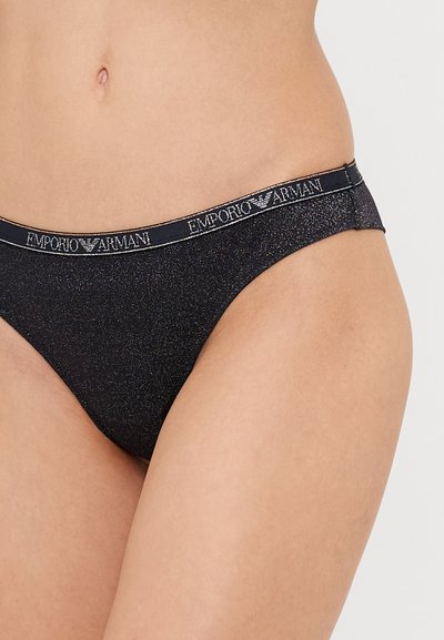 Crne, sjajne tange s kontrastnim pojasom koji sadrži "Emporio Armani" logo u srebrnoj boji. Glatka tkanina, minimalna pokrivenost.