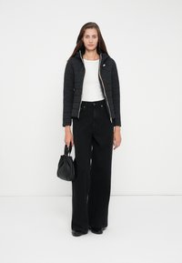 Quiltet svart jakke med glidelås og hette, kombinert med høywaistrede sorte jeans og en liten svart håndveske. Hvit topp under.