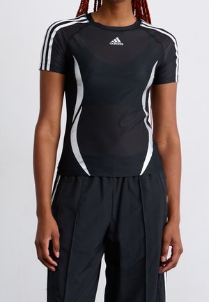 Personne portant un t-shirt de sport Adidas noir à manches courtes avec des bandes blanches sur les épaules et les côtés, associé à un pantalon noir.