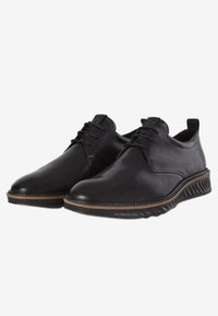 Scarpe in pelle nera con una texture liscia, design con lacci e suola a contrasto marrone. Presentano una punta rotonda e dettagli di cucitura minimi.