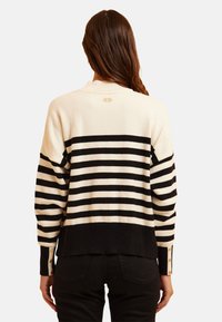 Maglione a righe in crema e nero, con maniche lunghe e dettagli con bottoni sui polsini. Collo a coste, texture morbida e vestibilità rilassata.