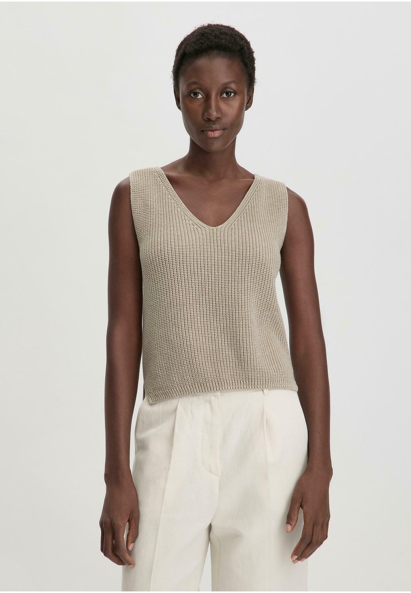 Top senza maniche beige a maglia con scollatura a V; presenta un motivo testurizzato e una vestibilità ampia, abbinato a pantaloni color crema.